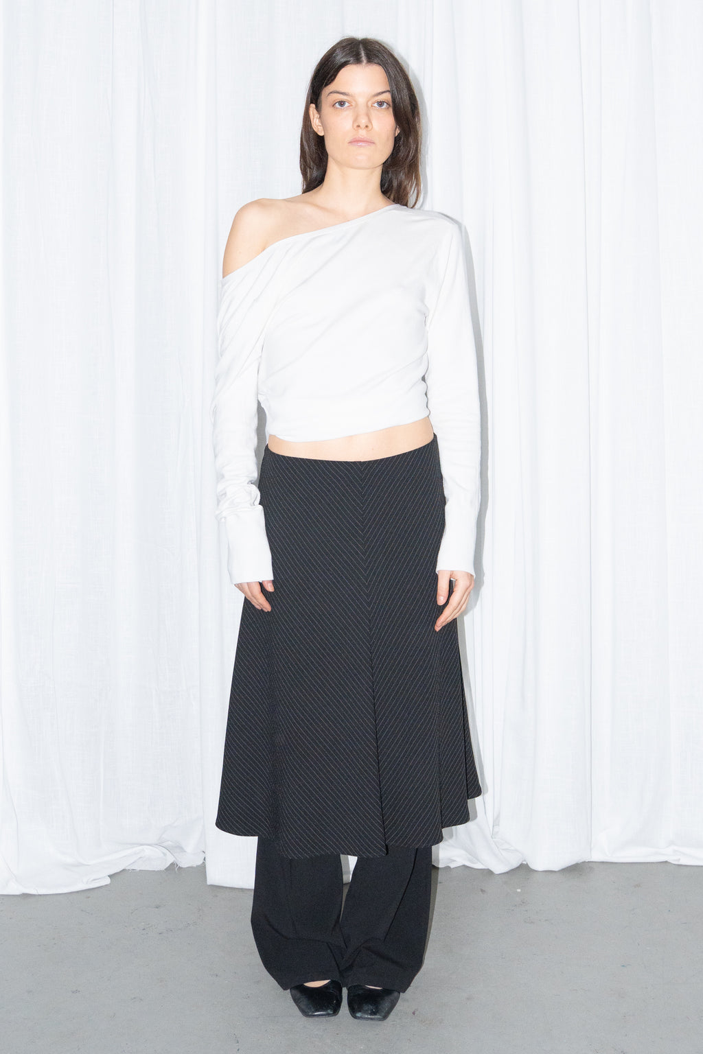 Model wearing a white off-shoulder cardigan with a black and grey diagonal pinstripe midi skirt over black trousers