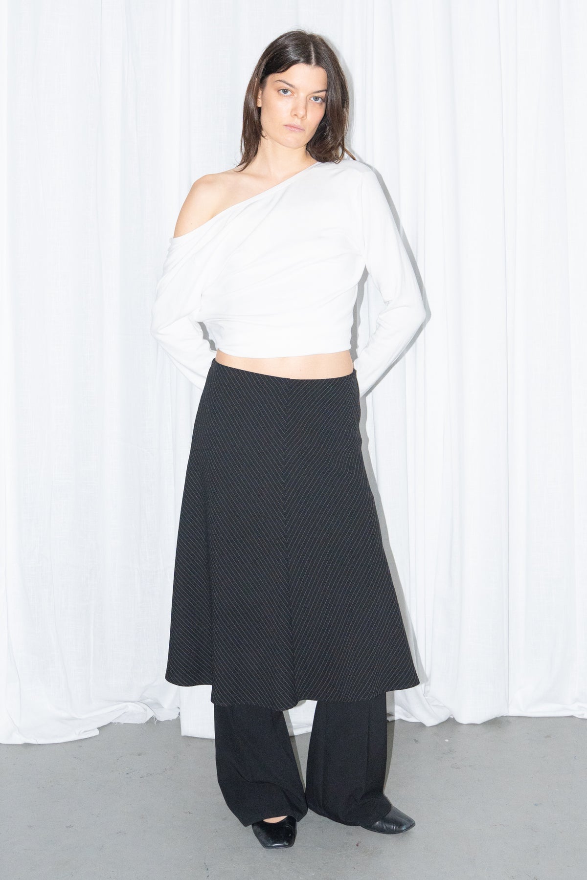 Model wearing a white off-shoulder cardigan with a black and grey diagonal pinstripe midi skirt over black trousers