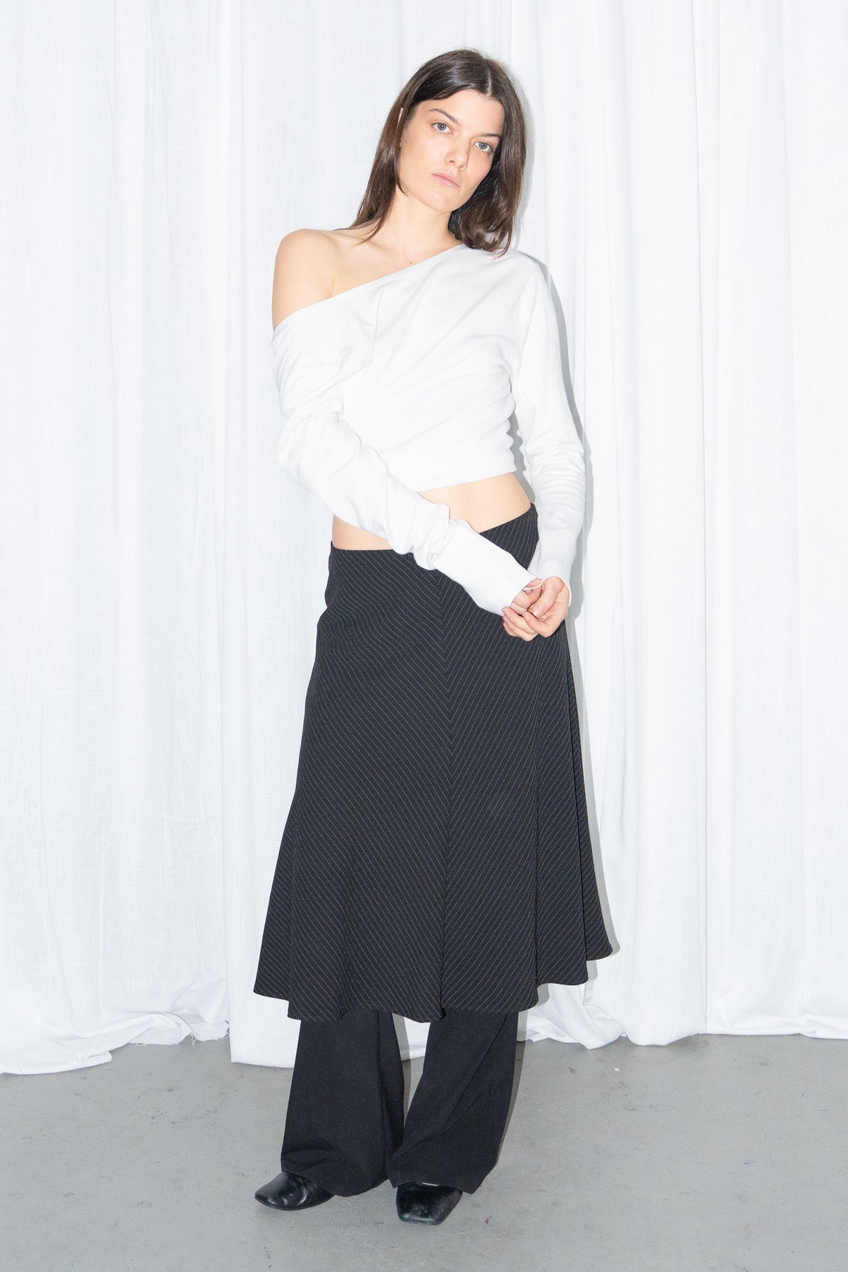 Model wearing a white off-shoulder cardigan with a black and grey diagonal pinstripe midi skirt over black trousers