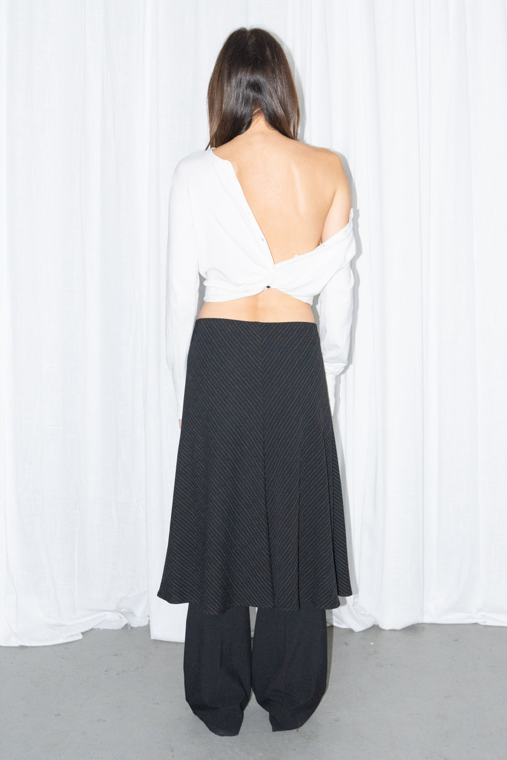 Back view of a white off-shoulder cardigan with a black and grey diagonal pinstripe midi skirt over black trousers