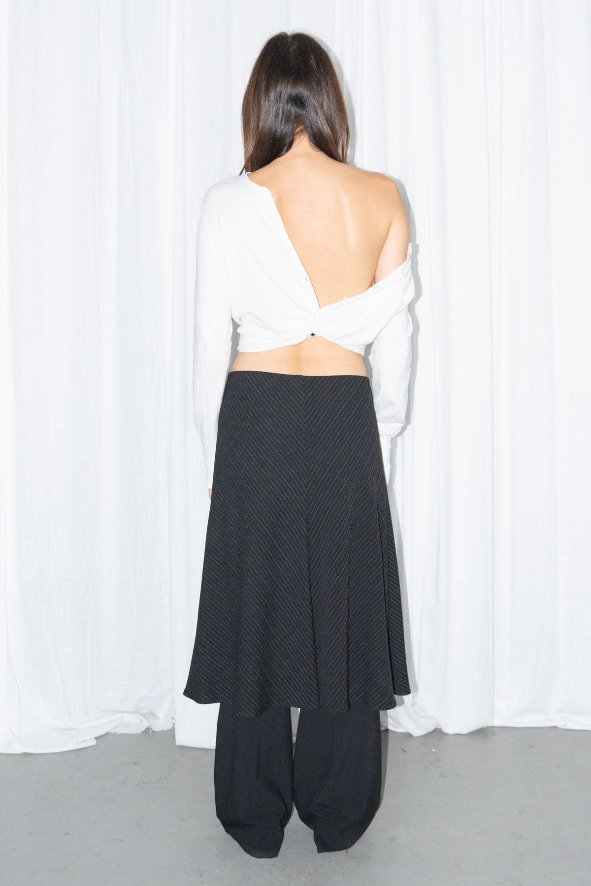 Back view of a white off-shoulder cardigan with a black and grey diagonal pinstripe midi skirt over black trousers