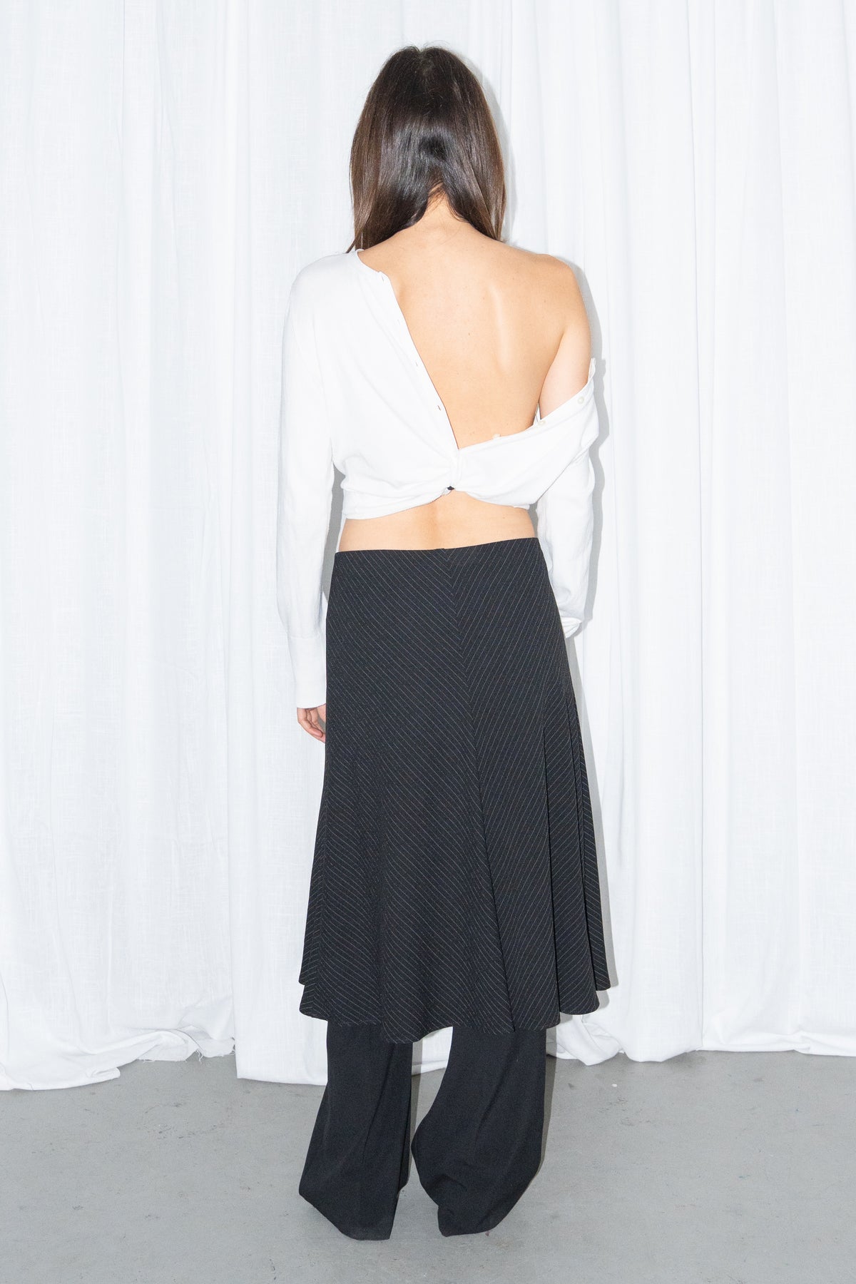 Back view of a white off-shoulder cardigan with a black and grey diagonal pinstripe midi skirt over black trousers