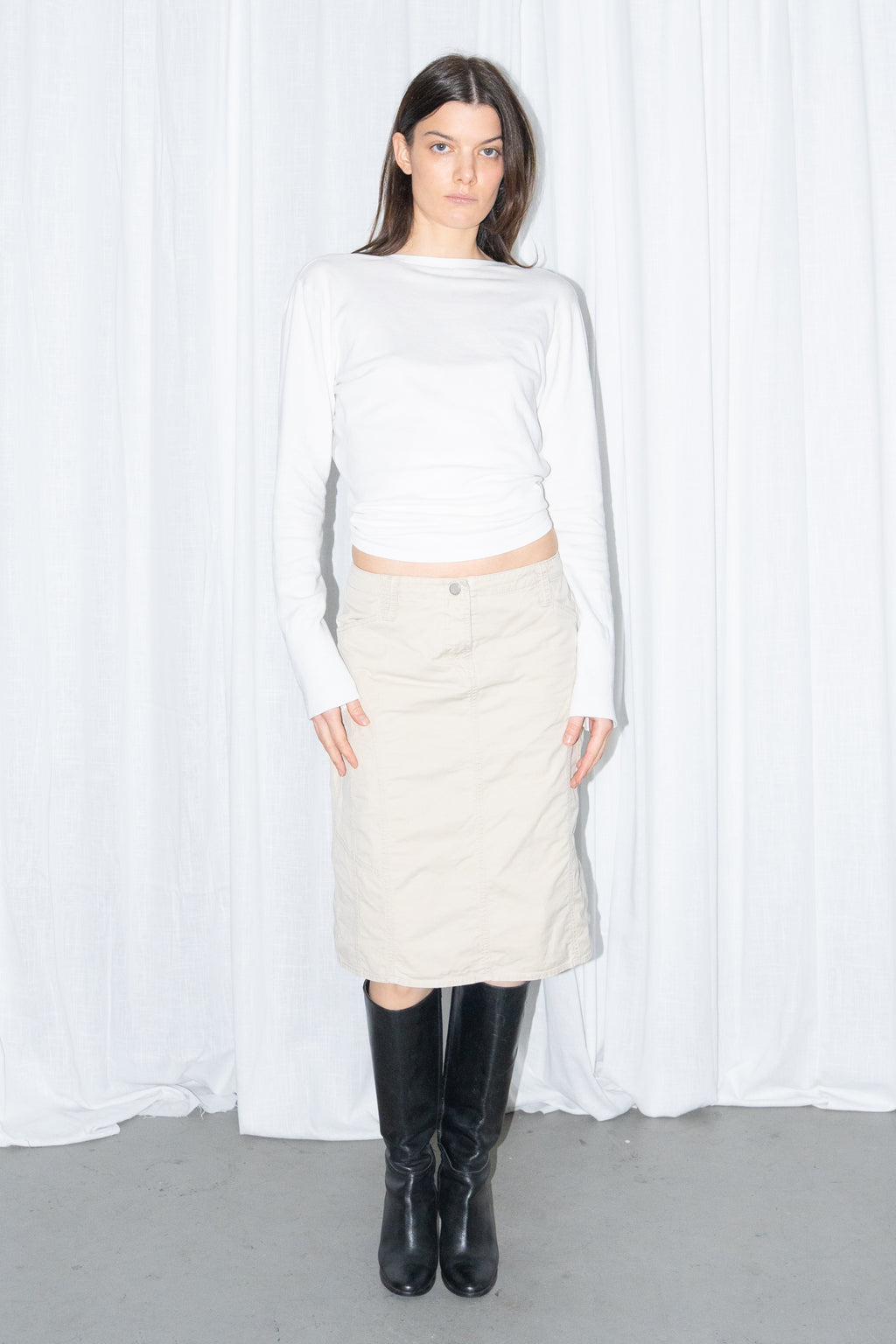 Model wearing a white cardigan with a beige midi skirt and black knee boots