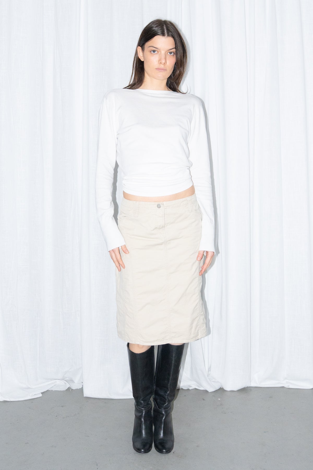 Model wearing a white cardigan with a beige midi skirt and black knee boots