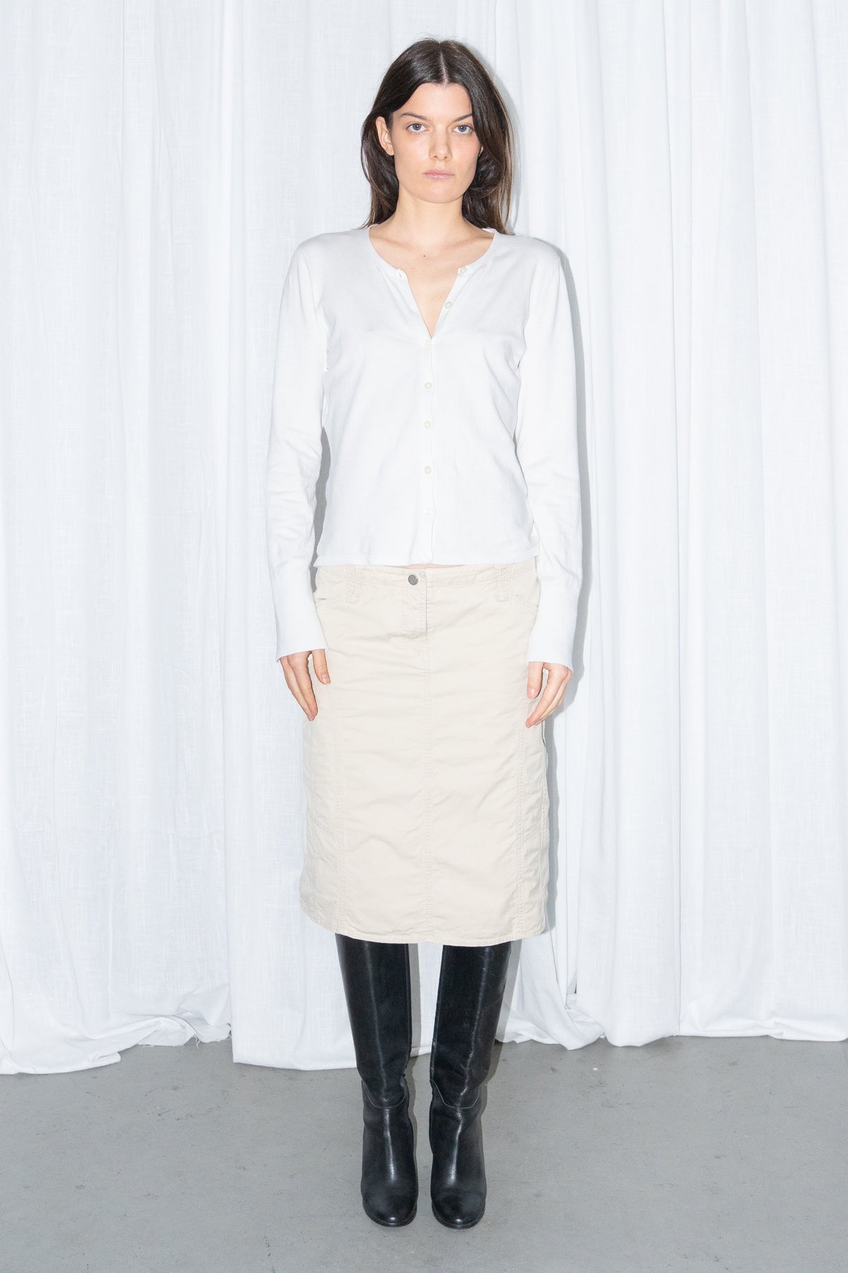 Model wearing a white cardigan with a beige midi skirt and black knee boots