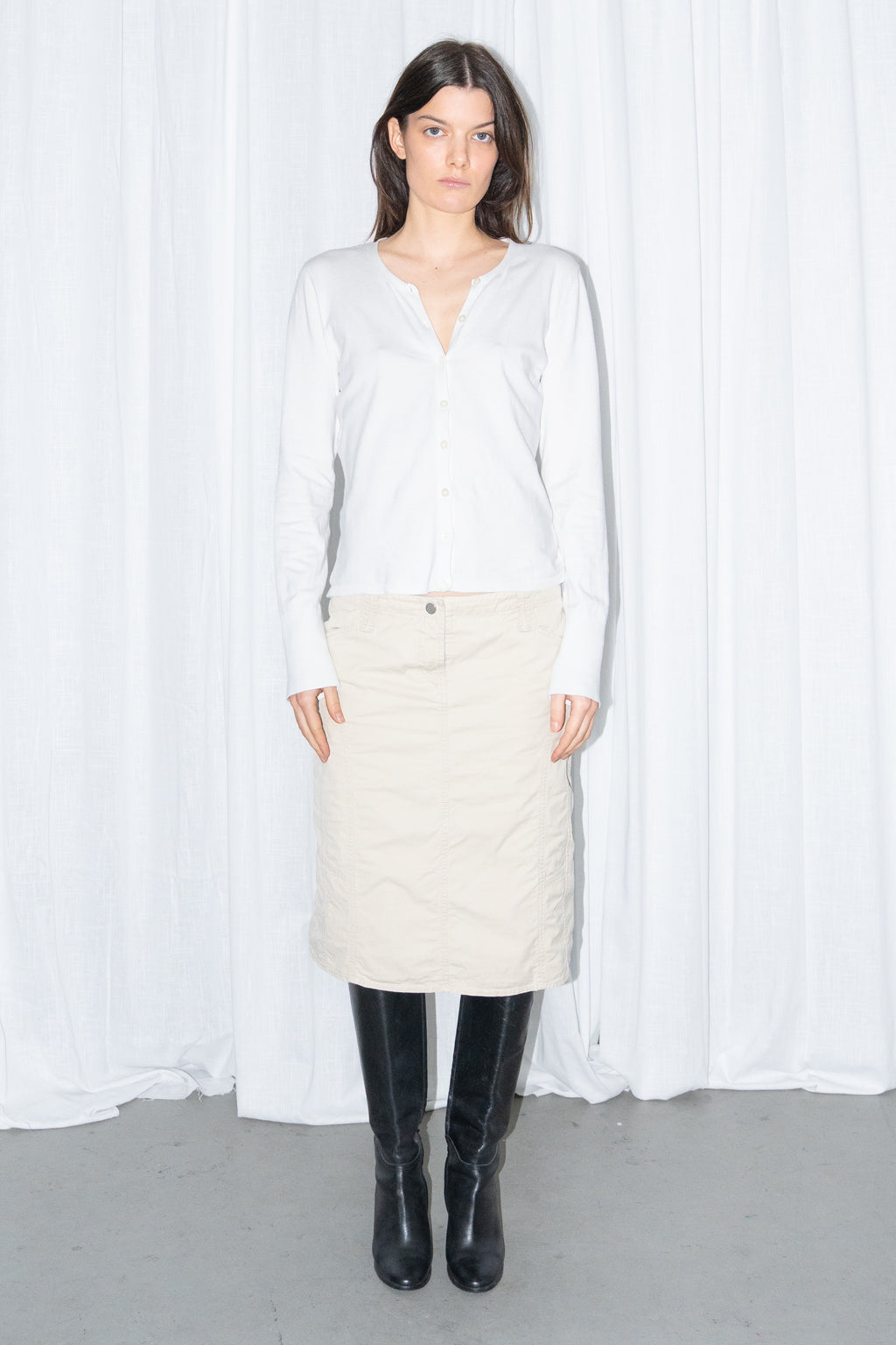 Model wearing a white cardigan with a beige midi skirt and black knee boots