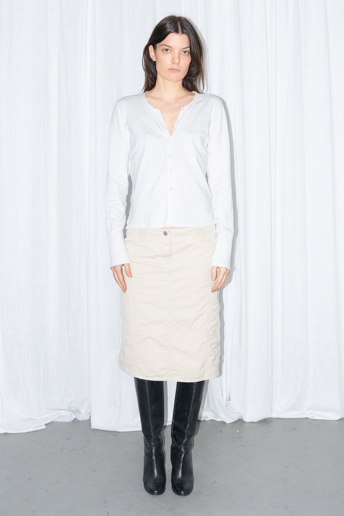 Model wearing a white cardigan with a beige midi skirt and black knee boots