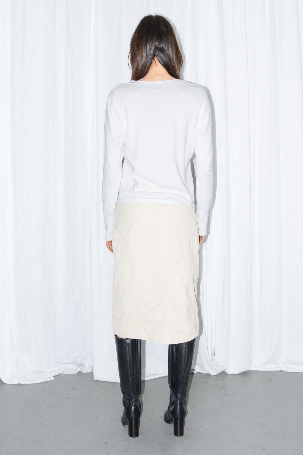 Back view of a white cardigan with a beige midi skirt and black knee boots