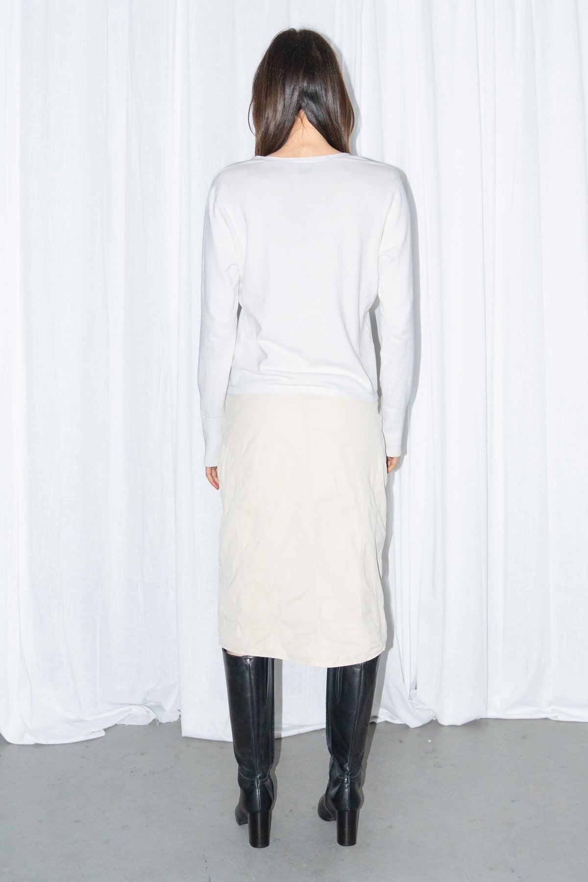 Back view of a white cardigan with a beige midi skirt and black knee boots
