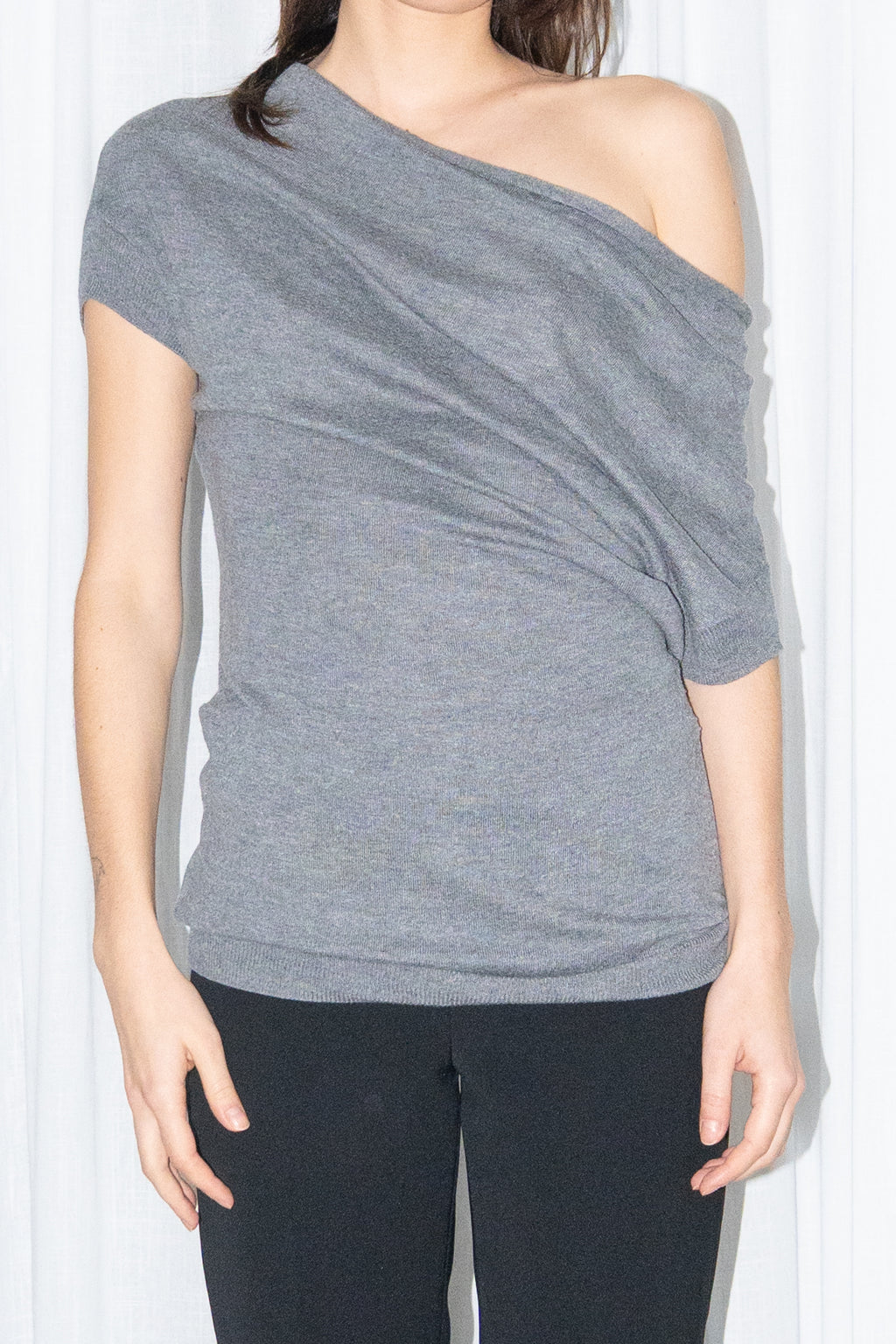 Close-up of a grey off-shoulder draped jersey knit top with a grey leather belt and black high-waist trousers