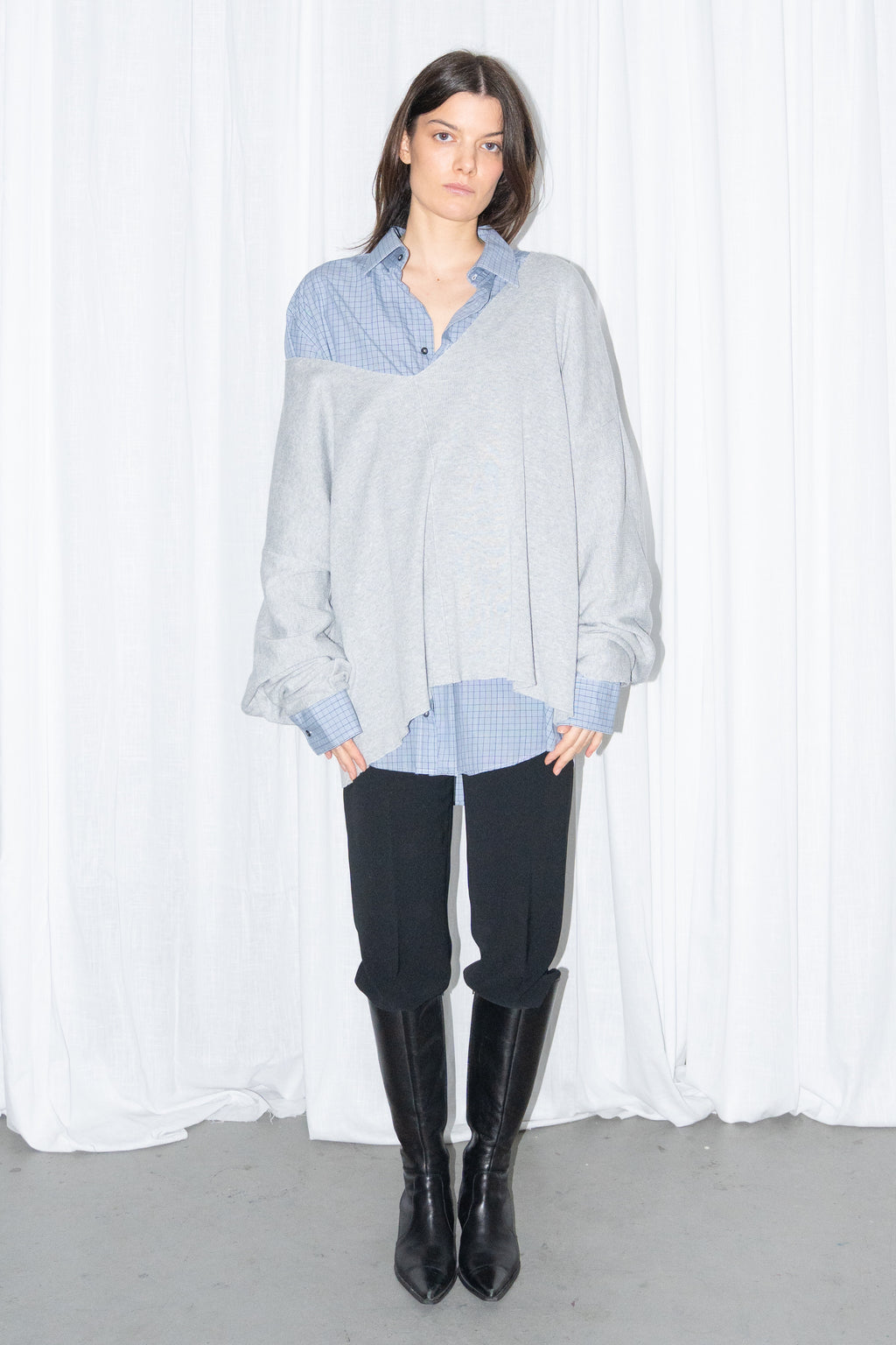 Front view of a light grey oversized V-neck knit sweater over a light blue shirt with black jeans and knee boots