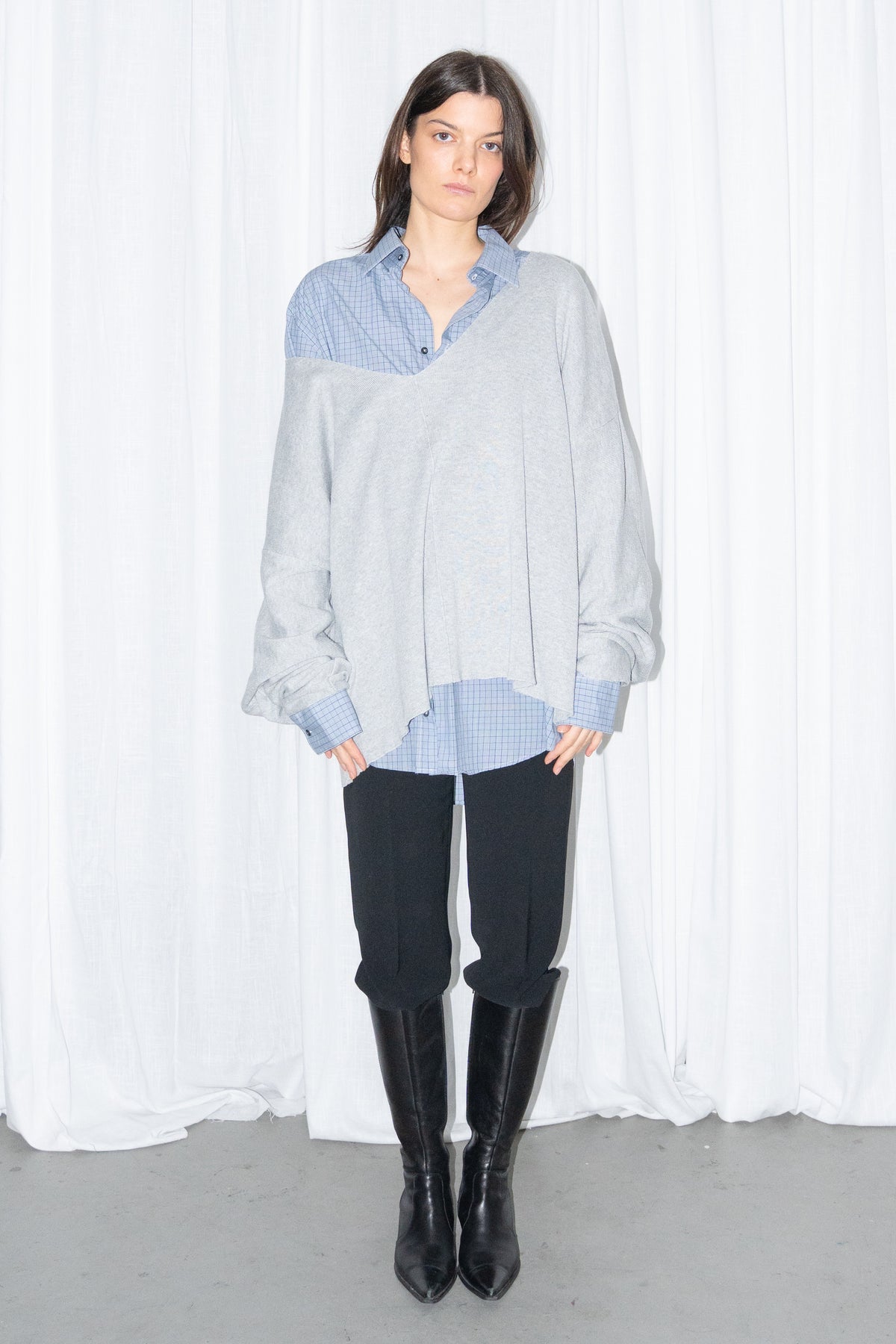 Front view of a light grey oversized V-neck knit sweater over a light blue shirt with black jeans and knee boots