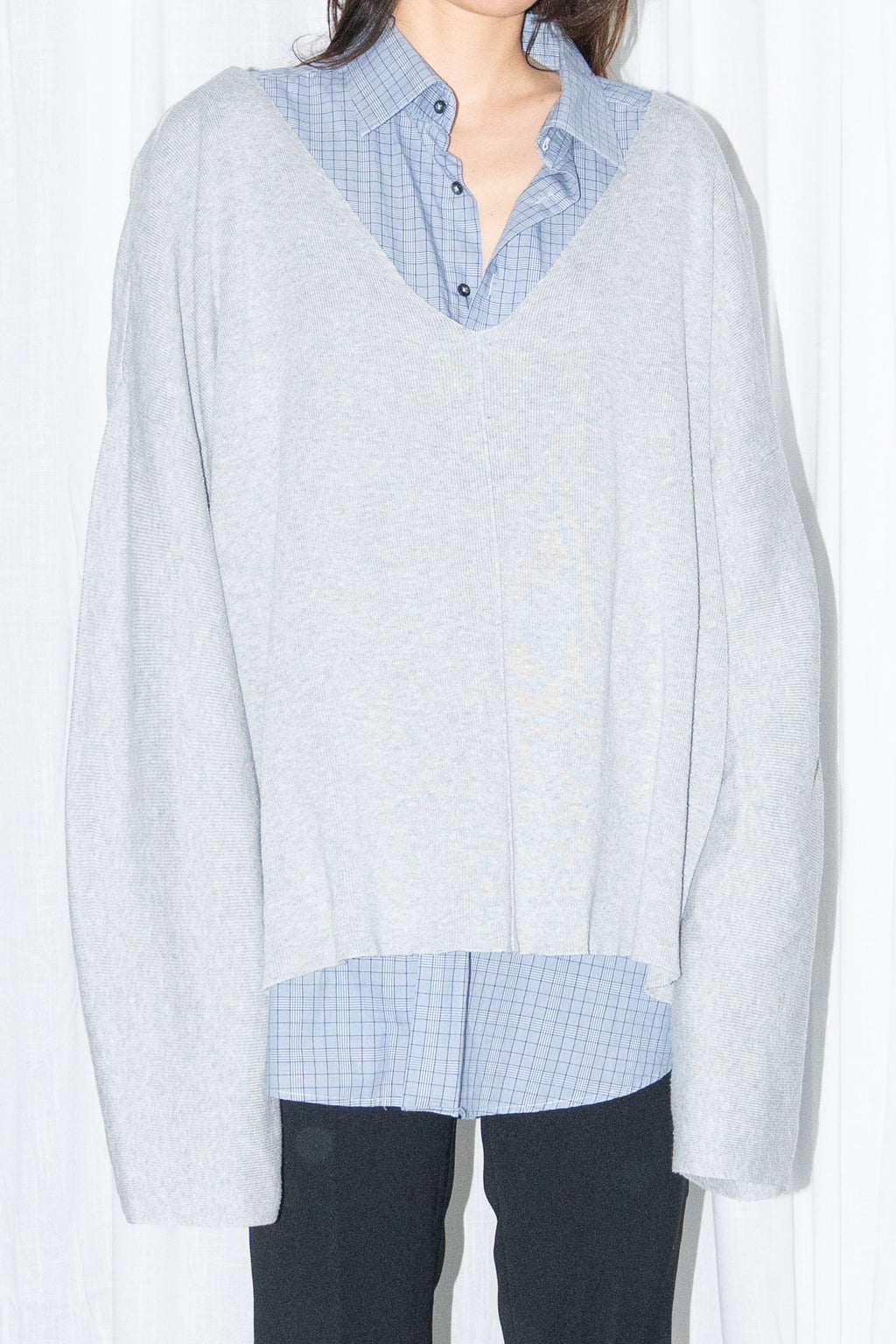 Close-up of a light grey oversized V-neck knit sweater over a light blue shirt with black jeans and knee boots