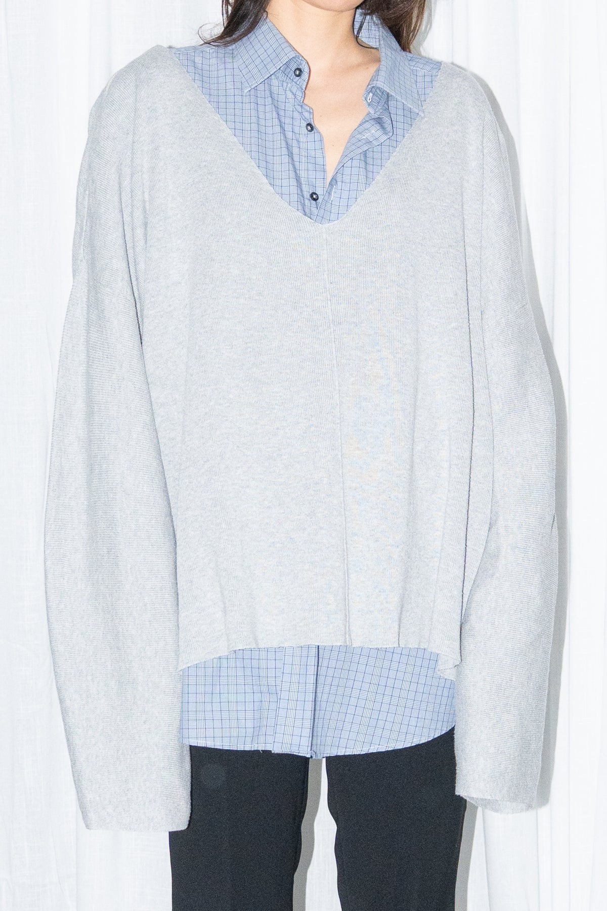 Close-up of a light grey oversized V-neck knit sweater over a light blue shirt with black jeans and knee boots