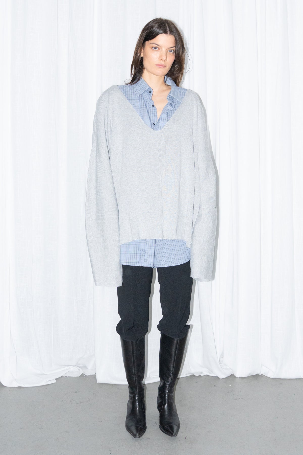 Front view of a light grey oversized V-neck knit sweater over a light blue shirt with black jeans and knee boots