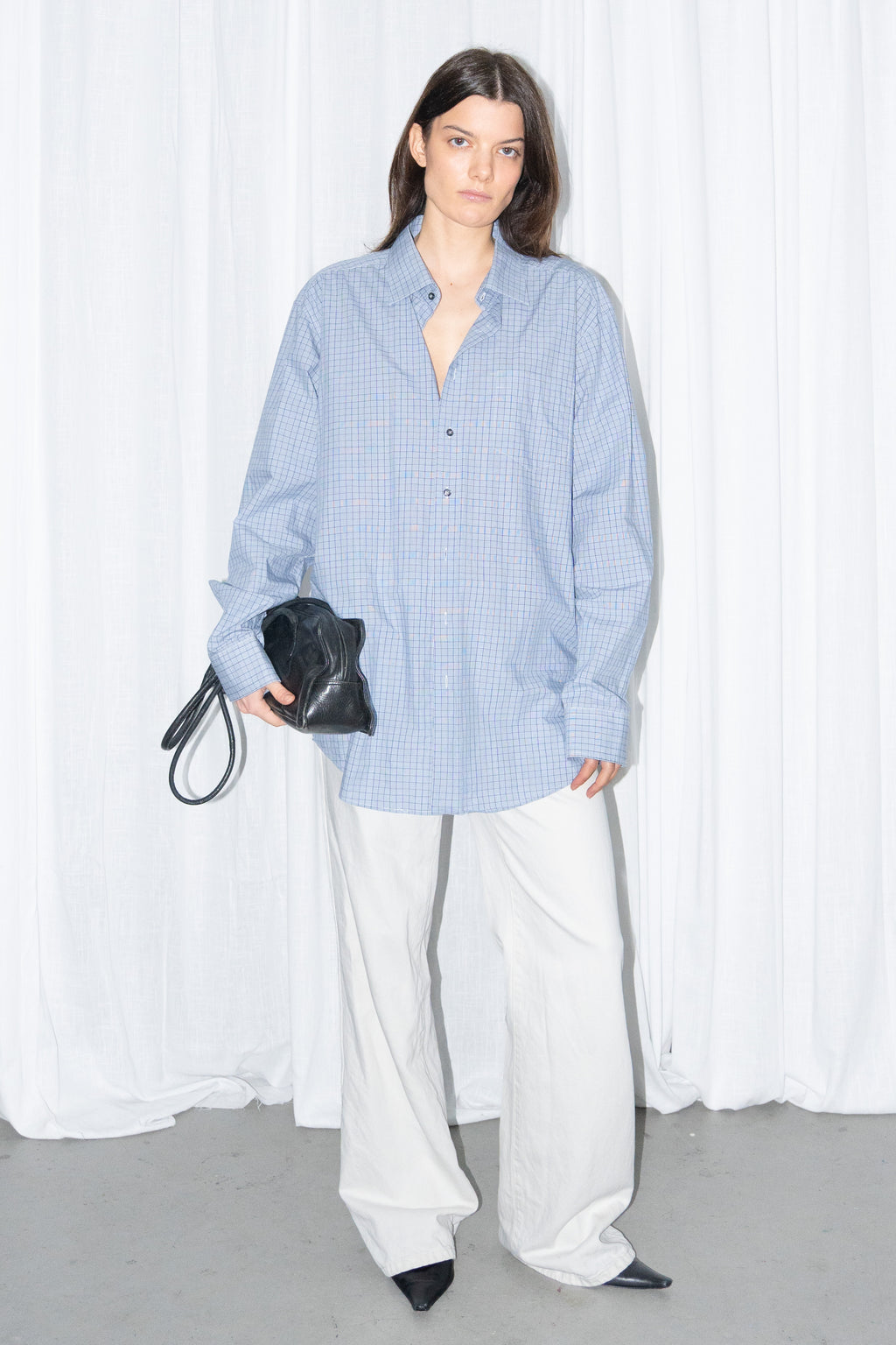 Model wearing a light blue oversized button-up shirt with white wide-leg trousers