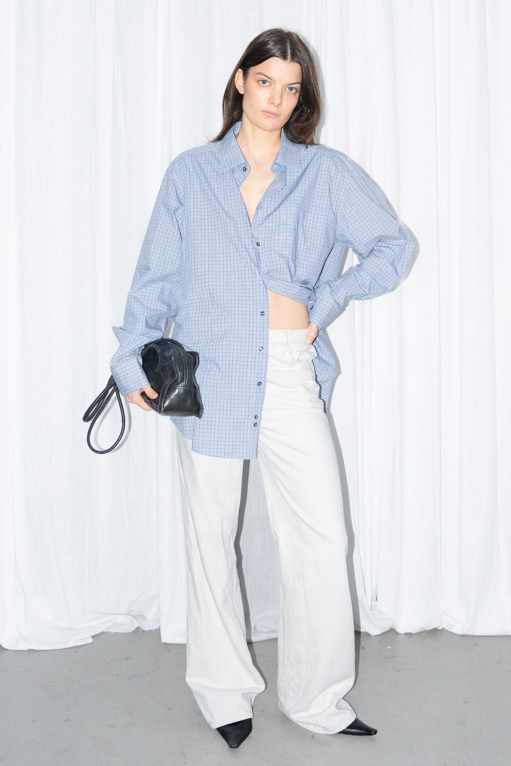 Model posing in a light blue oversized button-up shirt with white wide-leg trousers