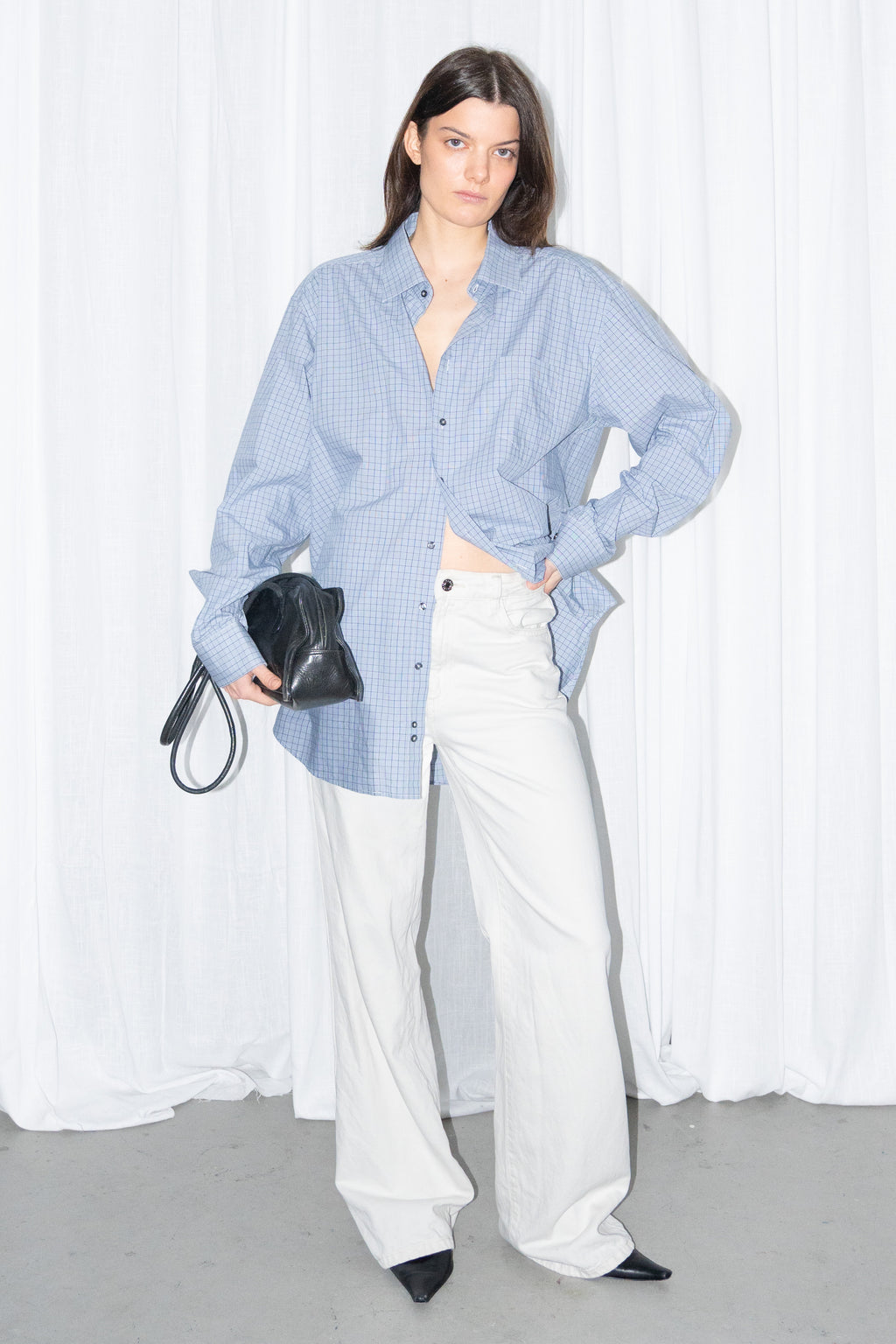 Model posing in a light blue oversized button-up shirt with white wide-leg trousers