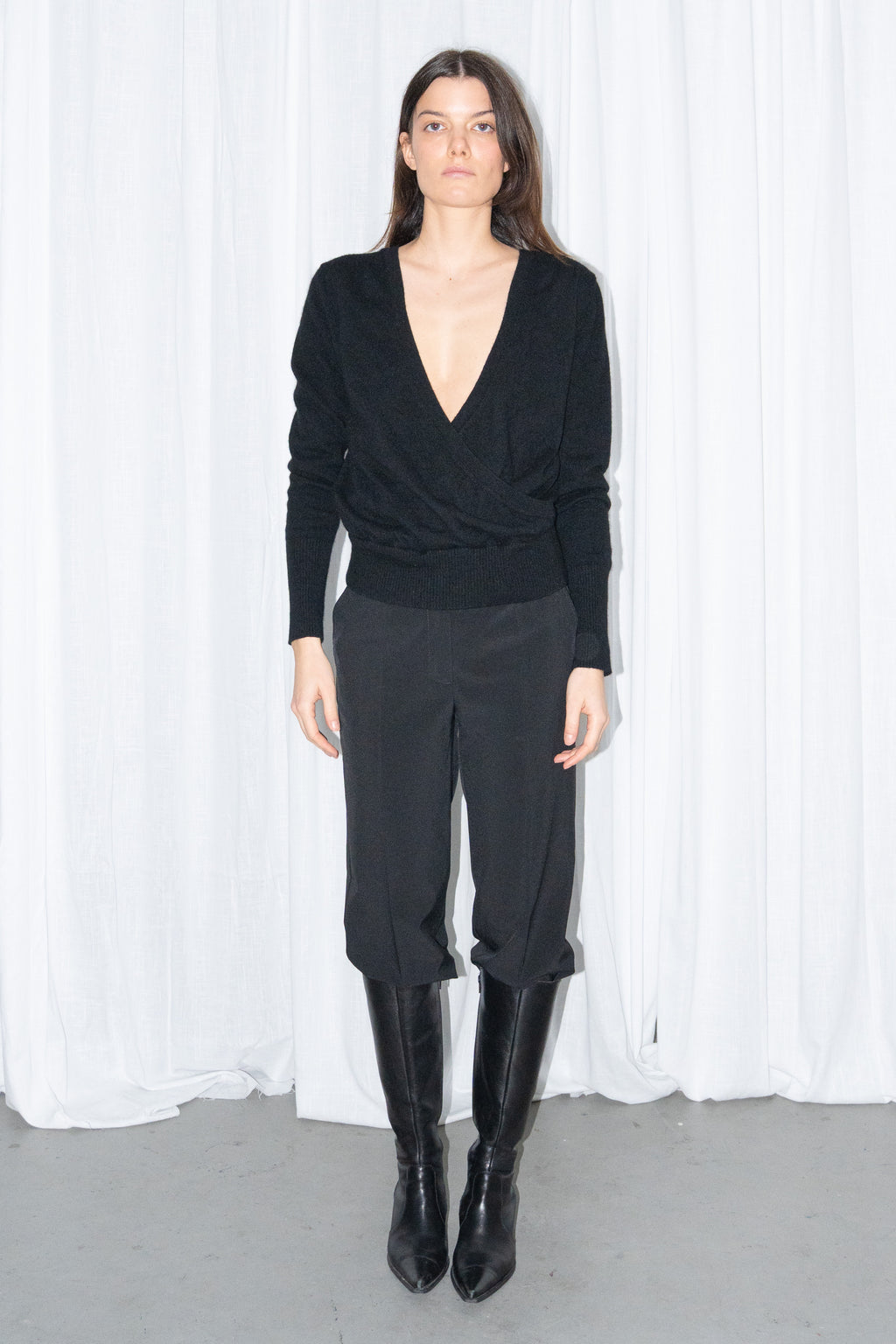 Model wearing a black cashmere wrap V-neck knit top with black high-waist trousers