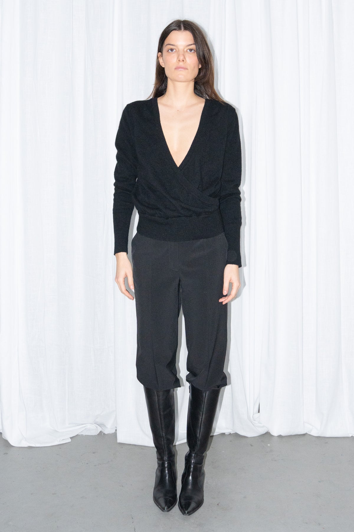 Model wearing a black cashmere wrap V-neck knit top with black high-waist trousers