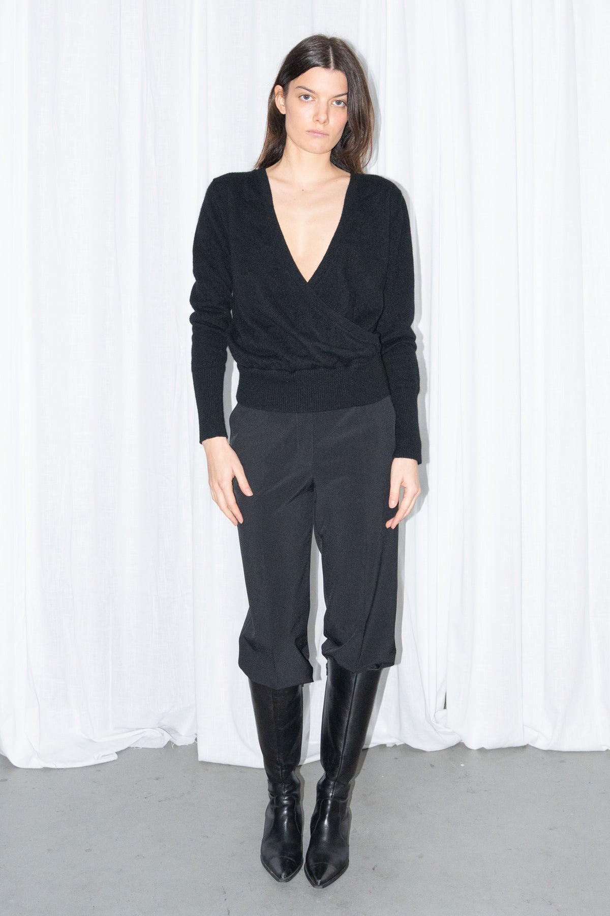 Model wearing a black cashmere wrap V-neck knit top with black high-waist trousers