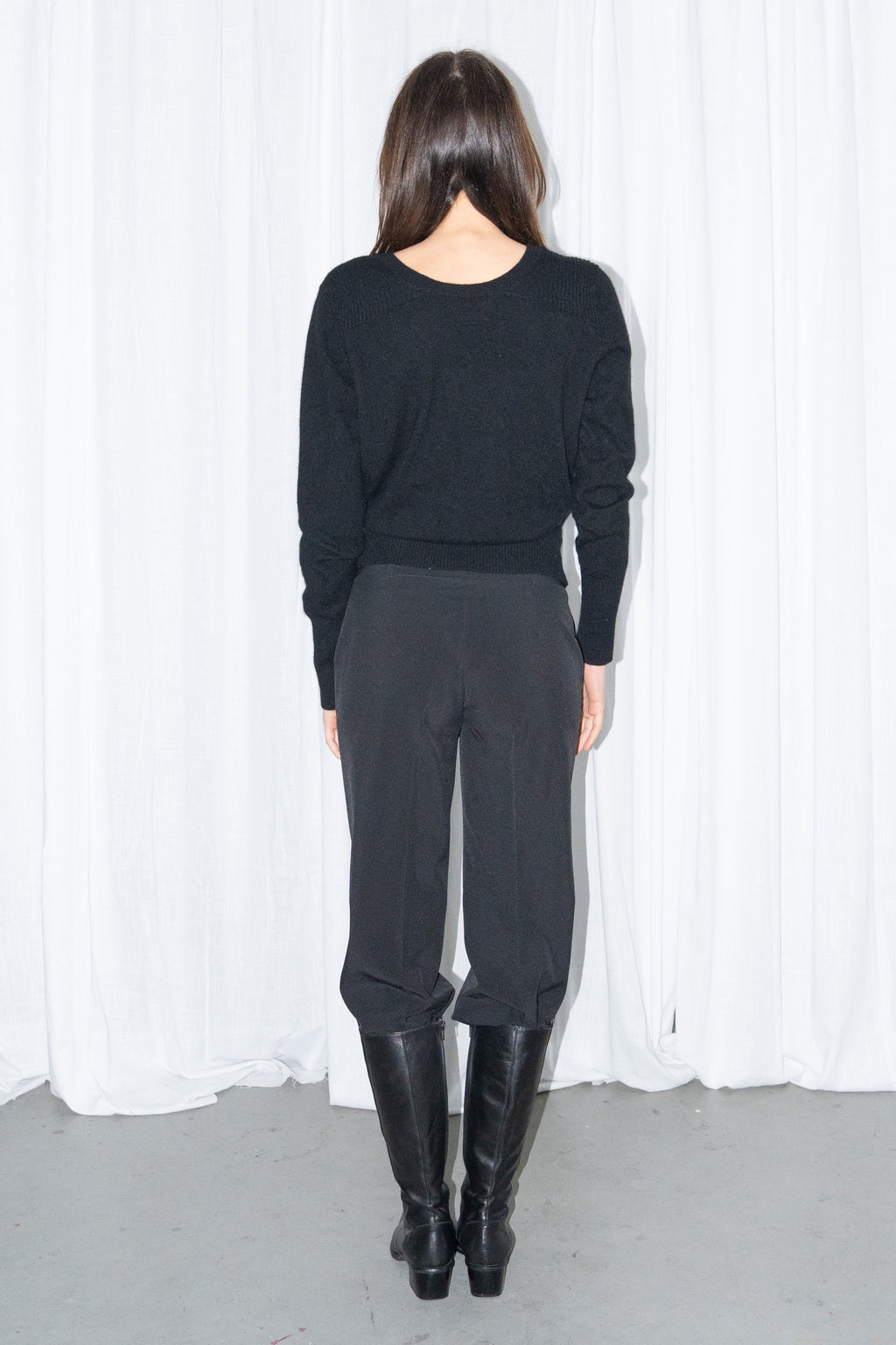 Back view of a black cashmere wrap V-neck knit top with black high-waist trousers