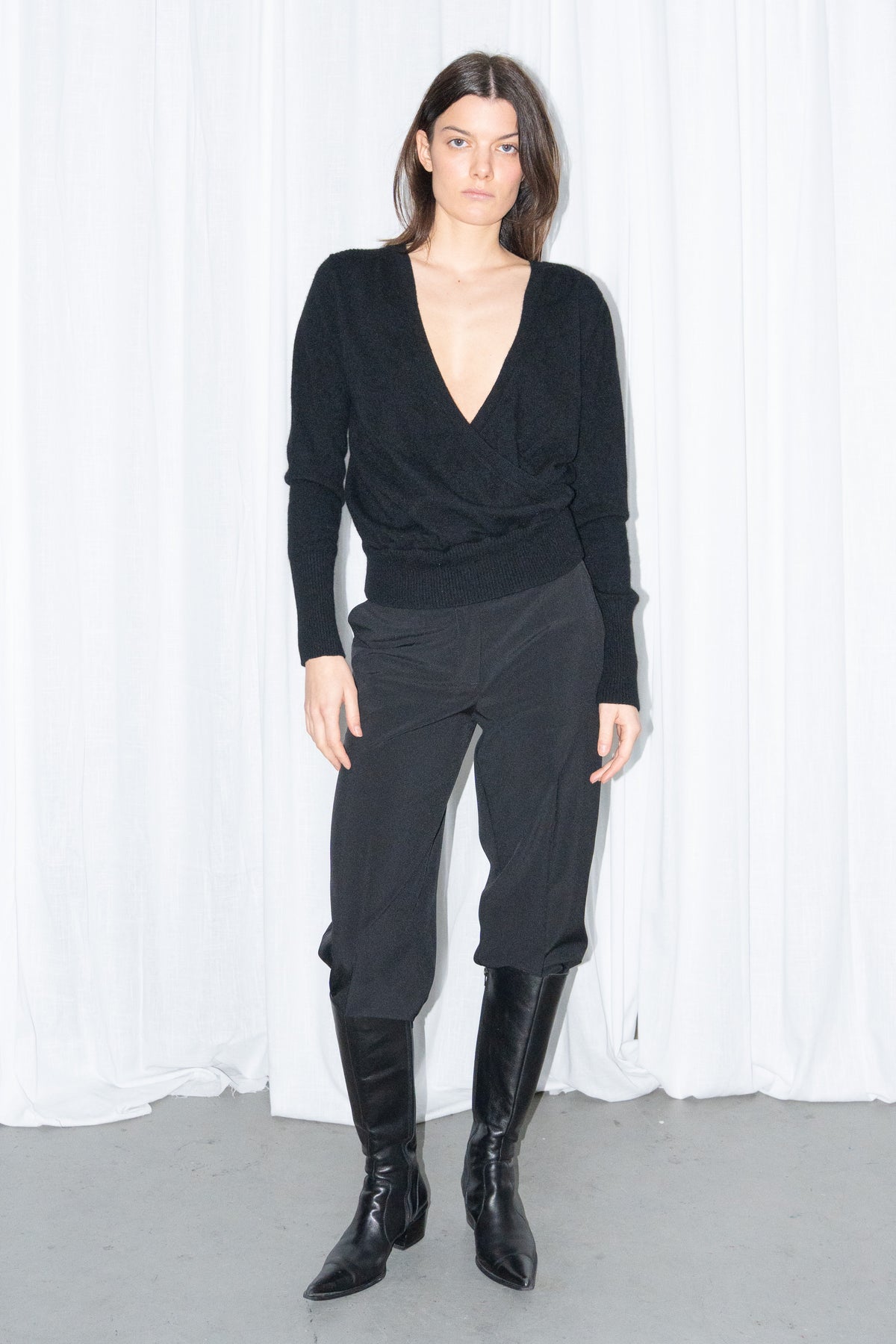 Model wearing a black cashmere wrap V-neck knit top with black high-waist trousers