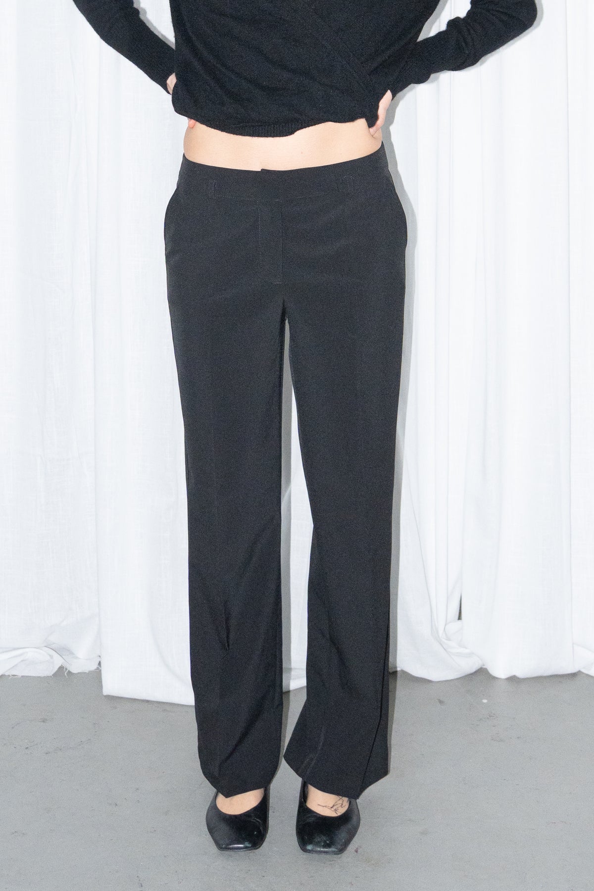 Close-up of black tailored straight trousers worn with a black chunky knit cardigan
