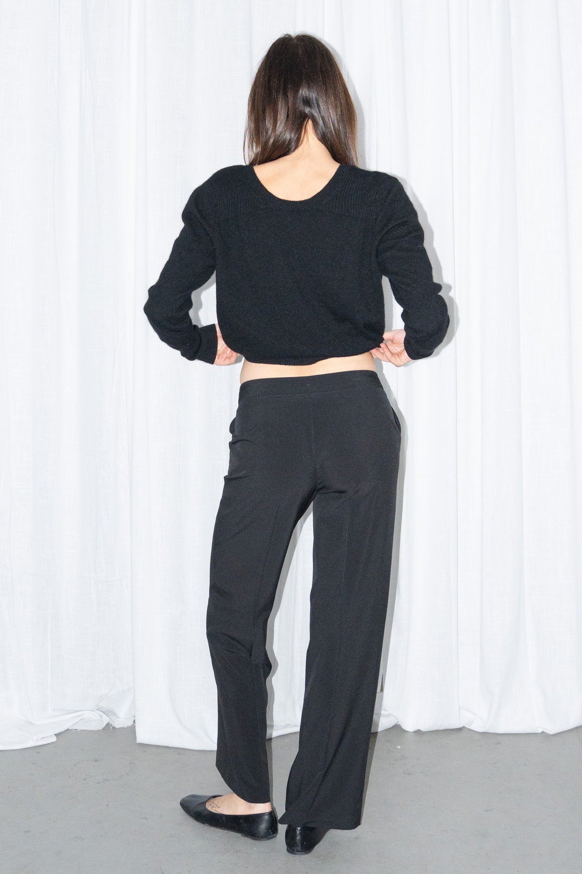 Back view of black tailored straight trousers with a black chunky knit cardigan
