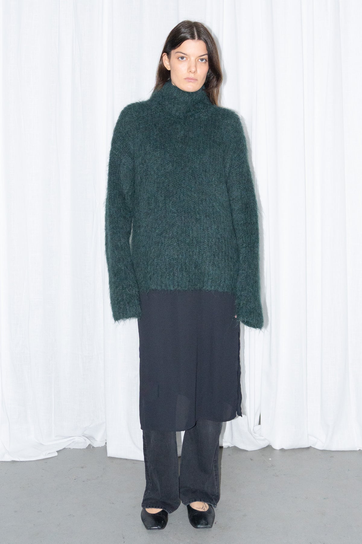 Model wearing dark green fluffy alpaca and wool turtleneck sweater with a black midi skirt over black trousers – MINIFALDA