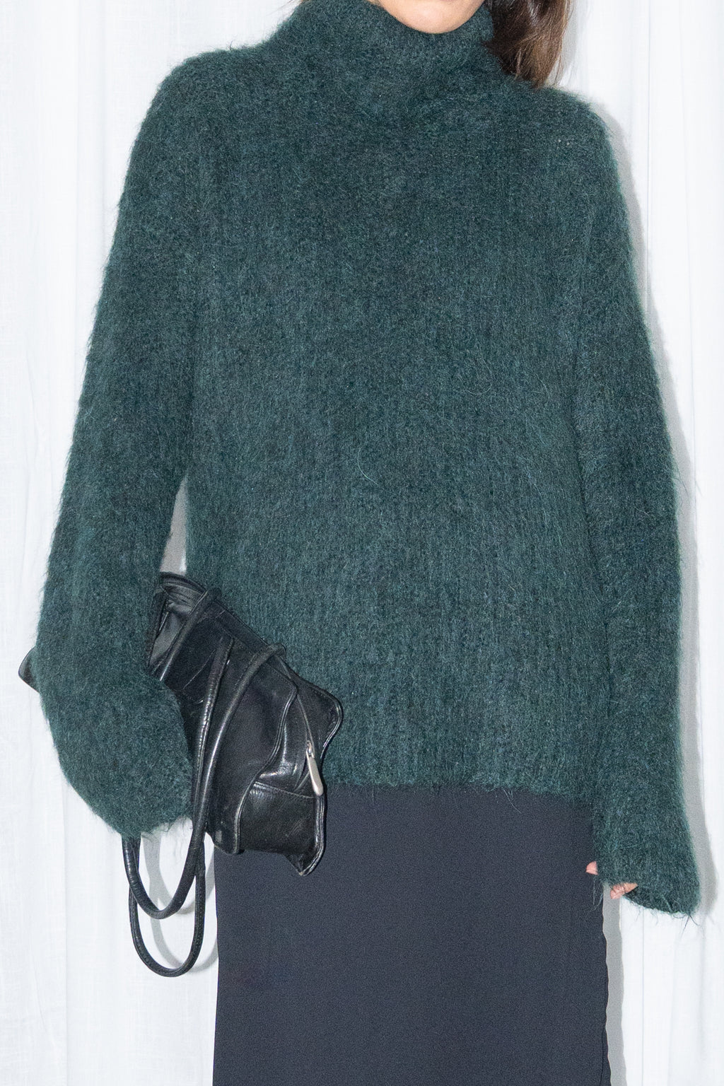 Close-up of dark green fluffy alpaca and wool turtleneck sweater with a black midi skirt over black trousers – MINIFALDA