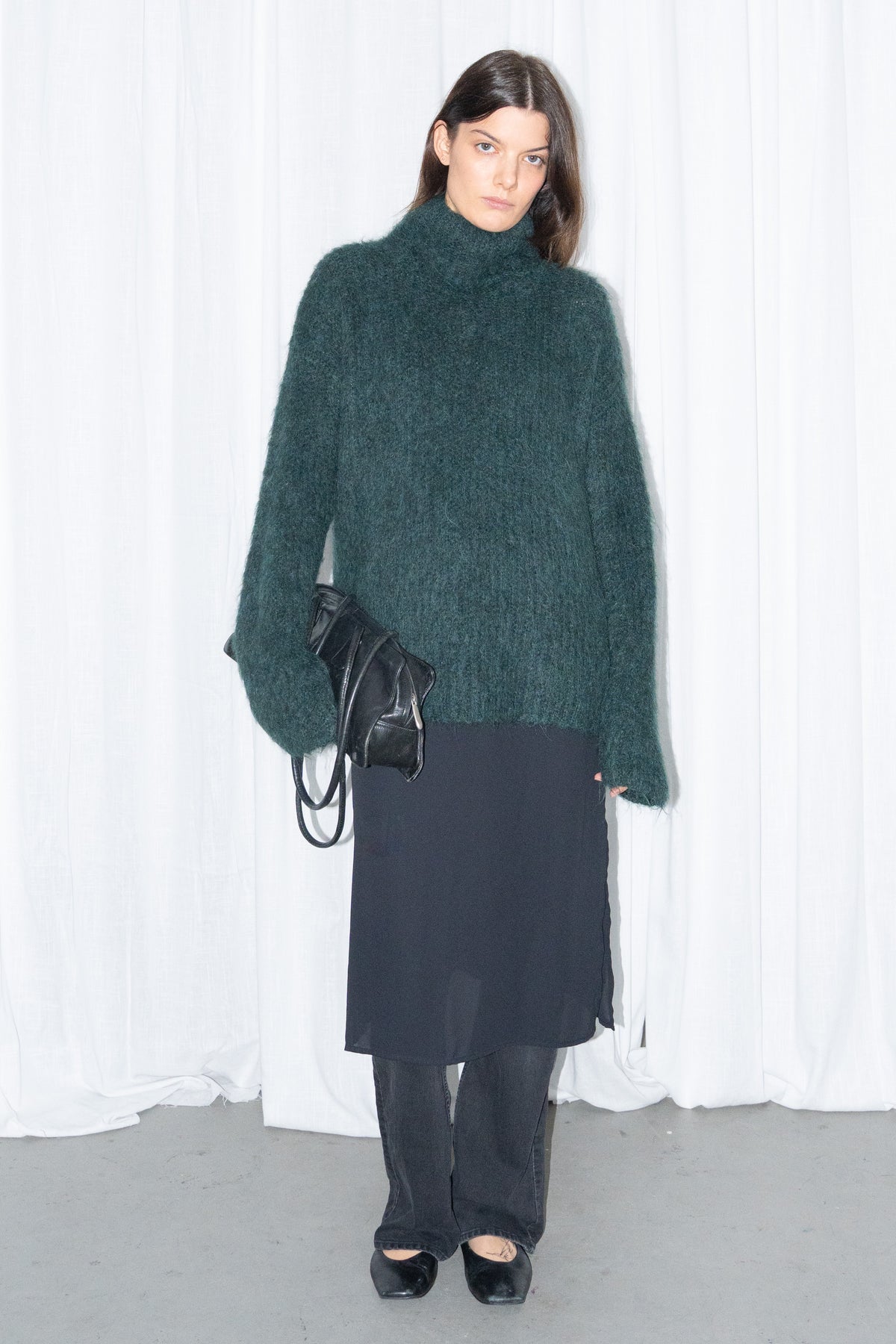 Model wearing dark green fluffy alpaca and wool turtleneck sweater with a black midi skirt over black trousers – MINIFALDA