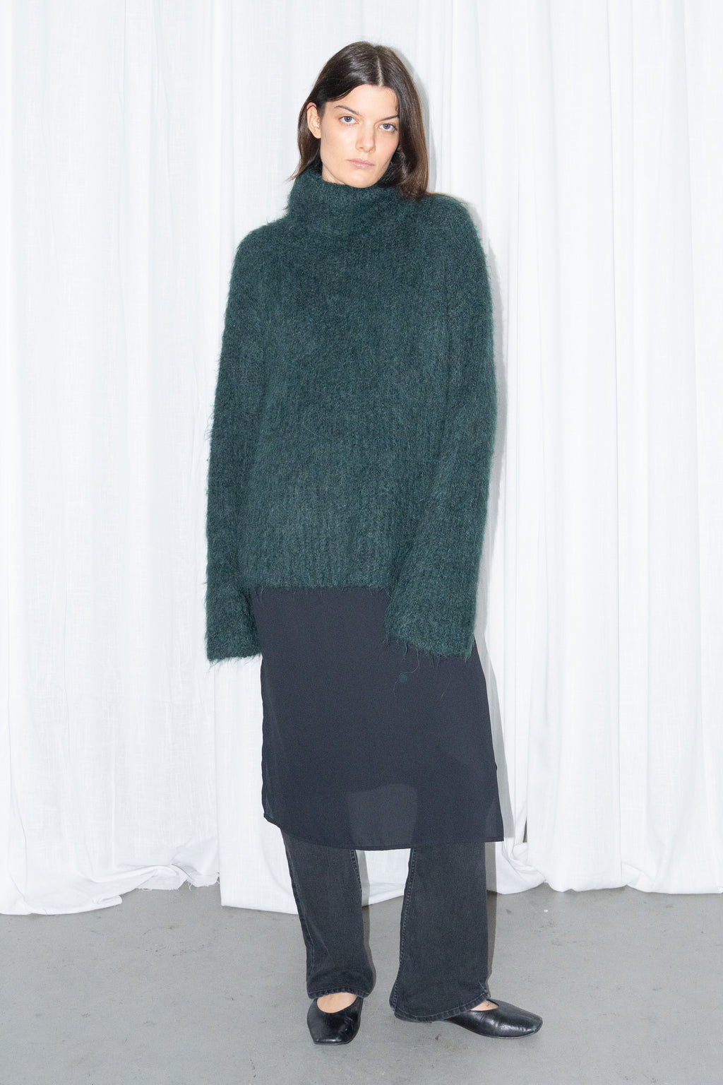 Model wearing dark green fluffy alpaca and wool turtleneck sweater with a black midi skirt over black trousers – MINIFALDA