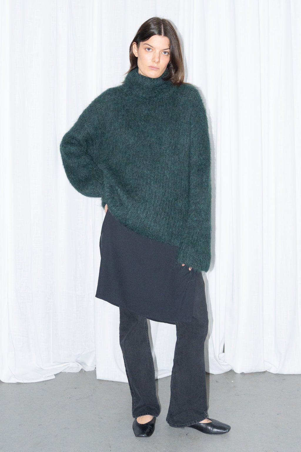 Model wearing dark green fluffy alpaca and wool turtleneck sweater with a black midi skirt over black trousers – MINIFALDA