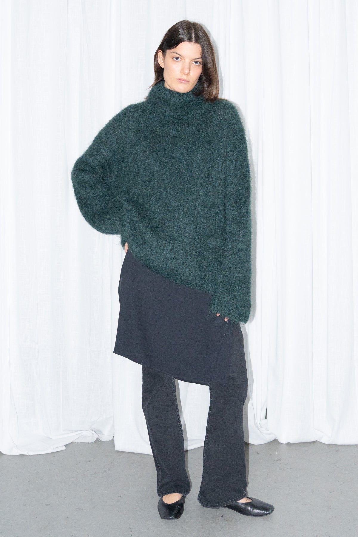 Model wearing dark green fluffy alpaca and wool turtleneck sweater with a black midi skirt over black trousers – MINIFALDA