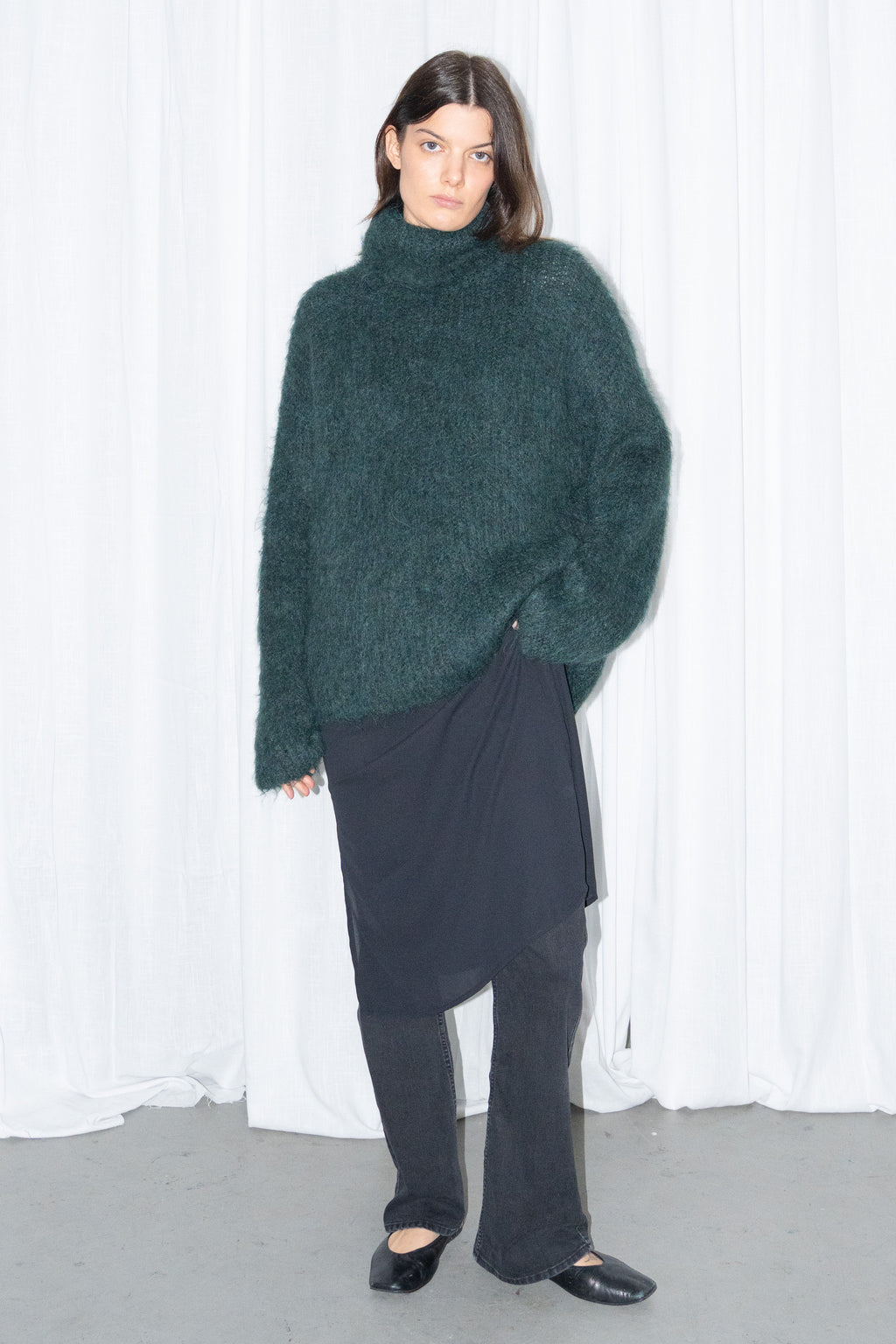 Model wearing dark green fluffy alpaca and wool turtleneck sweater with a black midi skirt over black trousers – MINIFALDA