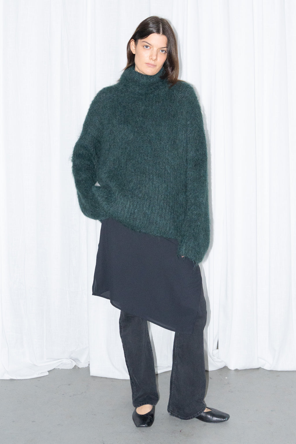 Model wearing dark green fluffy alpaca and wool turtleneck sweater with a black midi skirt over black trousers – MINIFALDA