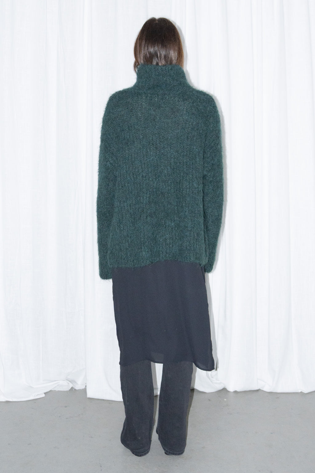 Model wearing dark green fluffy alpaca and wool turtleneck sweater with a black midi skirt over black trousers – MINIFALDA