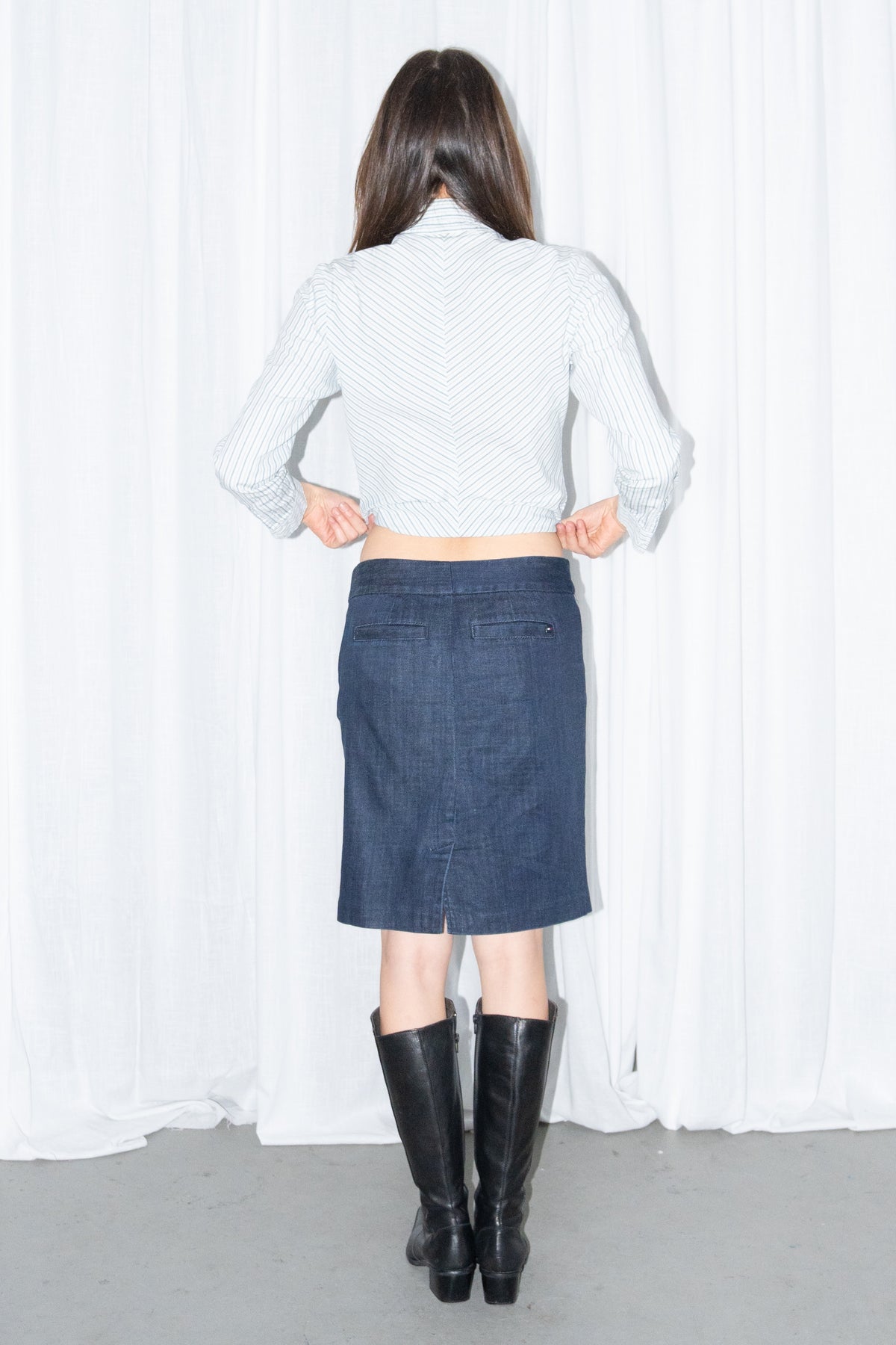Back view of a light blue striped fitted shirt with a dark blue denim knee-length skirt