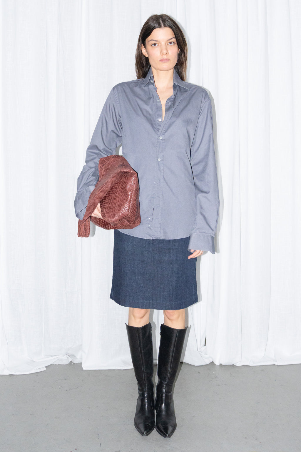 Model wearing a grey button-up shirt with a dark blue denim skirt and a burgundy leather bag