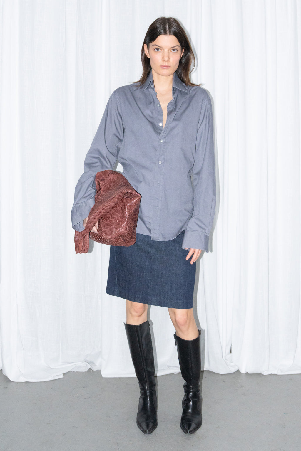 Model wearing a grey button-up shirt with a dark blue denim skirt and a burgundy leather bag